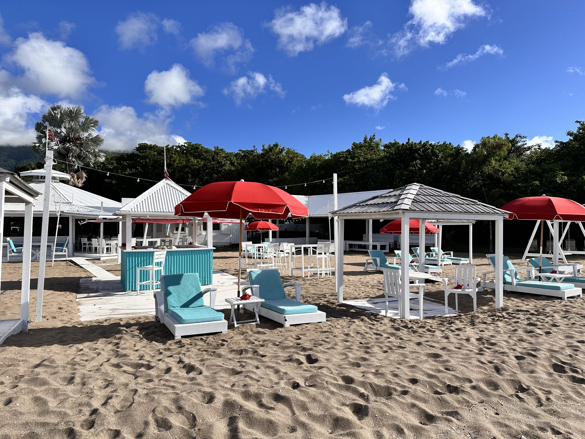 A beachfront club with red umbrellas and white cabanas on a sandy beach in Nevis