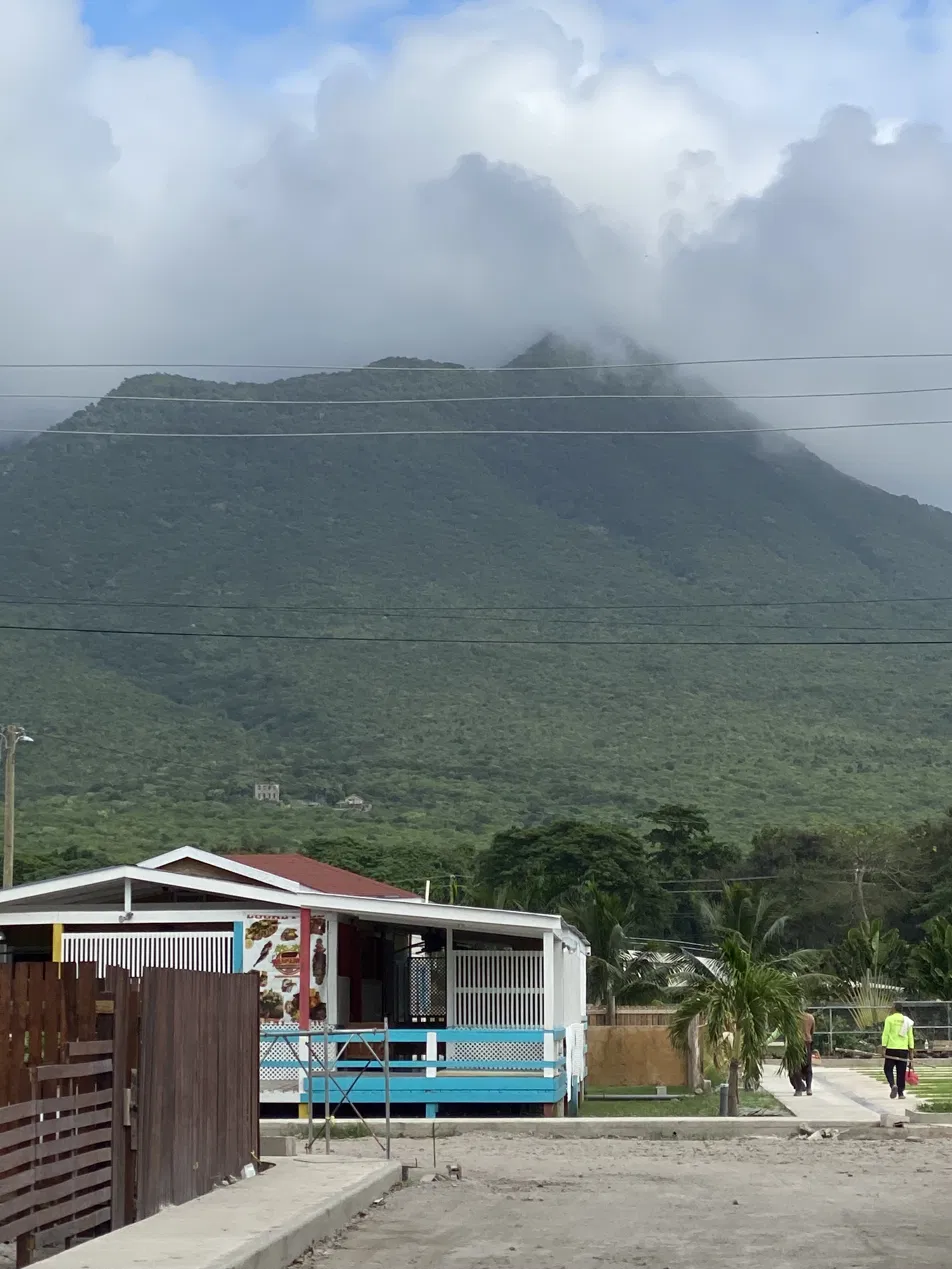 Nevis Peak wrapped in cloud, with a roadside food shack in the foregroundNevis Peak shrouded in cloud behind a roadside food shack, near the Hamilton Estate geothermal site